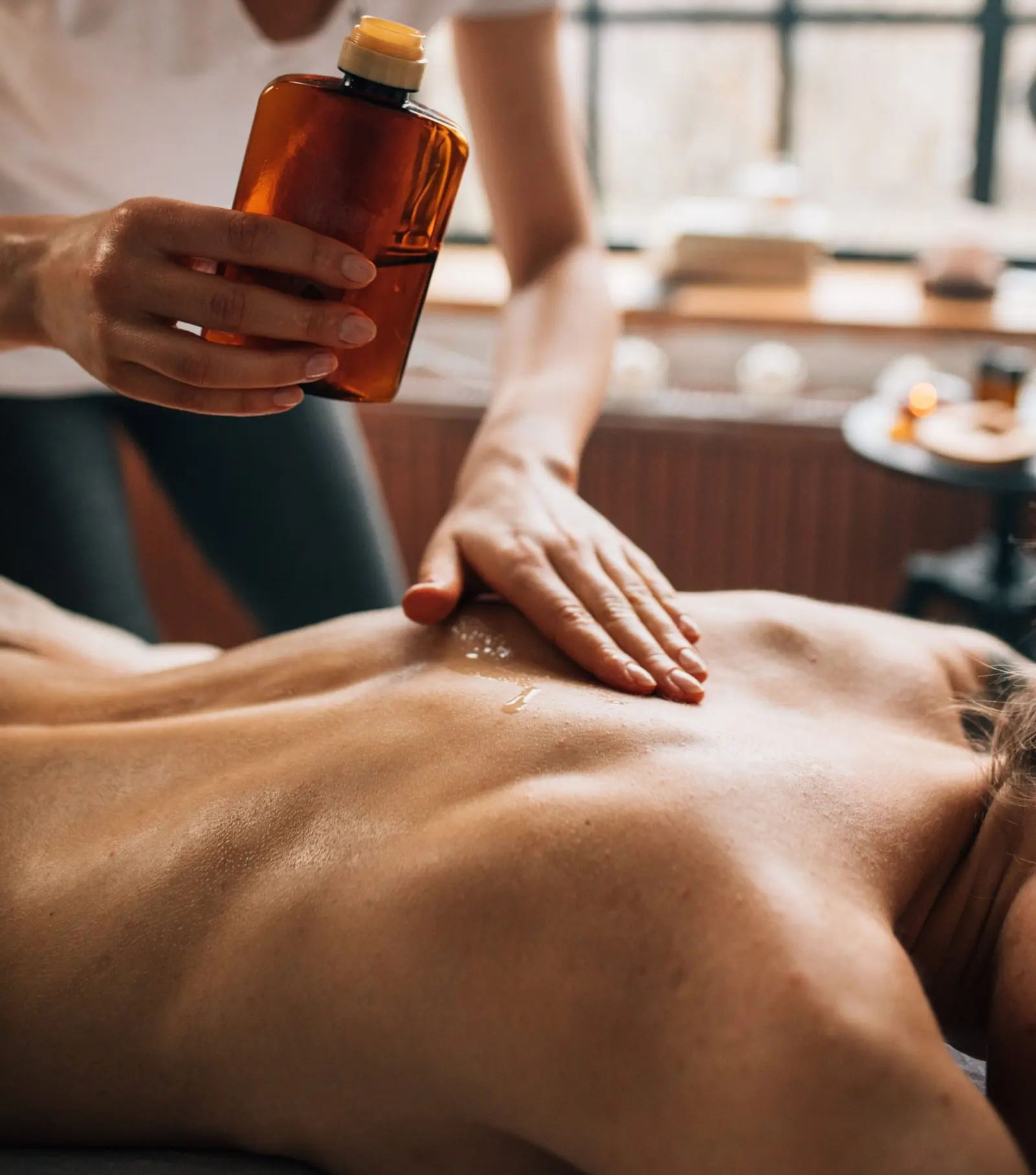Hand mit Massageöl auf dem Rücken einer liegenden Frau